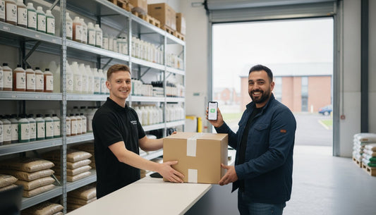 A warehouse worker handing a cardboard parcel to a customer holding a smartphone.